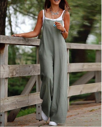 Woman wearing a stylish green fashion jumpsuit for women walking outdoors by a wooden fence